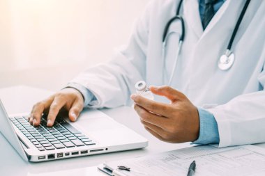 Doktor laptopla ilaç şişesini kontrol ediyor..
