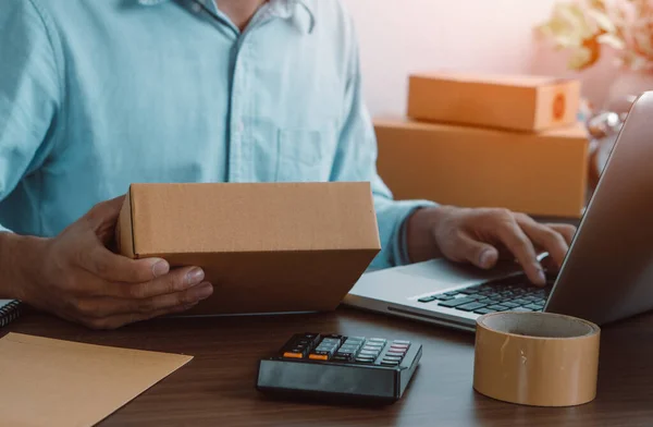 Adam çevrimiçi satıcı ürün paketini hazırlar ve müşteri adreslerini müşteriye teslim etmek için kontrol eder. Online satış, e-ticaret.