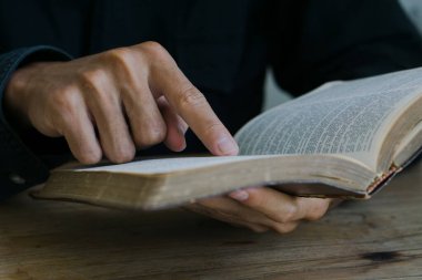 Hristiyan adam İncil okur. Elleri katlanmış, kutsal bir İncil 'in üzerinde, ahşap bir masanın üzerinde..