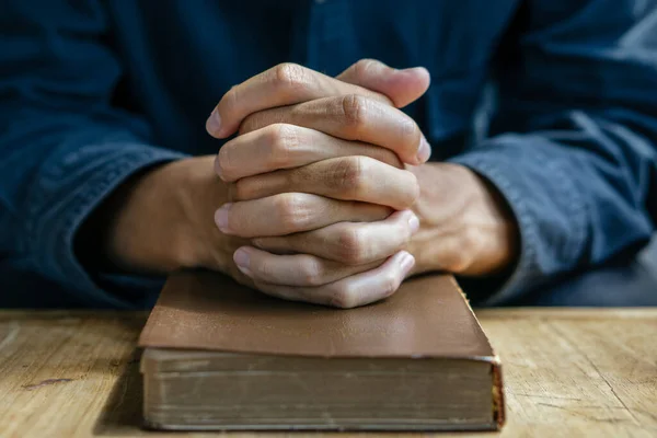 Christian man read bible. Hands folded in prayer on a Holy Bible on wooden table.
