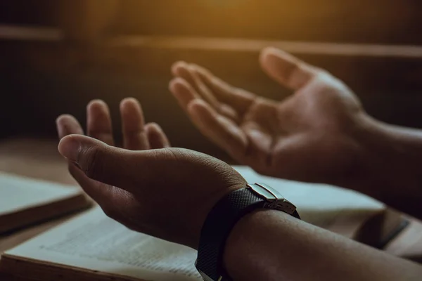 İncil 'de dua eden bir adamın elleri. Tanrı' ya dua eden bir Hıristiyan. İnsan Tanrı için dua eder. İyiliğe inanır. Tahta bir masada el ele tutuşup dua ediyoruz..
