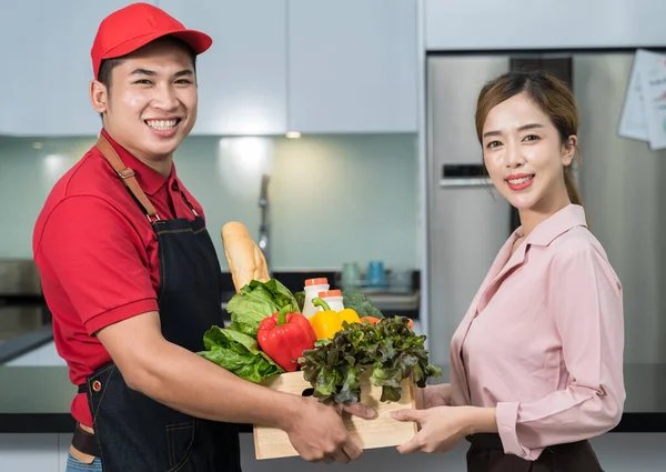 Staff from the grocery store send it to a female customer at the kitchen. Customer picks up fresh food from the grocery store ordered online from the courier in transportation and delivery concept