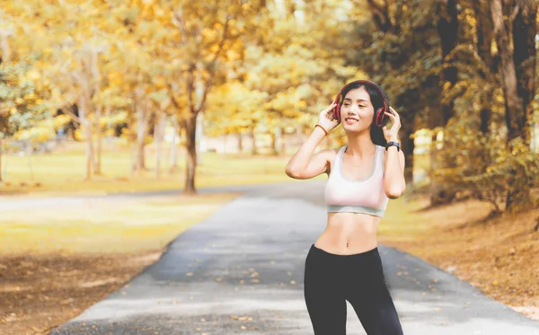 Healthy woman are listening to music during exercise in a happy and relaxing mood at the park with autumn leaves blur bokeh background and sunlight in sport and healthy concept with copy space