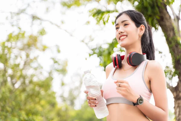 Asyalı kadınlar spor yapıyor ve parkta koşarken su şişesini ellerinde tutuyorlar, Asyalı kadınlar kilo vermek için maraton ya da kardiyo antrenmanı yapıyorlar ve park geçmişi olan sağlıklı bir konsept kullanıyorlar.