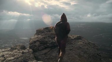 Doğadaki doğa gezisi konsepti. Kayalık dağın tepesinde yürüyen bir adamın arka görüntüsü. Dünyanın tepesinde özgürlüğün verdiği bir his. Yürüyüşçü doğal bir maceraya çıkar.