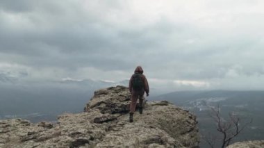 Zirveye giden yolu tamamlayan adamın küçük bir figürü zaferle sevinçle ellerini kaldırıyor. Yeni hedefleri fethetmek. Yolculuğun sonu. Gökyüzünde kasvetli bulutlar olan manzara.