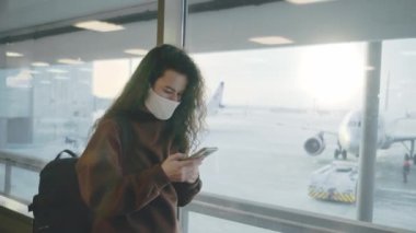 Elinde cep telefonu ve turist çantasıyla genç bir kadın pencerenin yanındaki havaalanında duruyor. Bilet kontrolü ya da çevrimiçi kayıt. Sınırların uluslararası turizme açılması