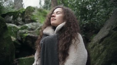 Kıvırcık saçlı kız derin bir nefes alır ya da temiz havada meditasyon yapar. Yeşil orman ve temiz çevre. Şehirden uzak temiz hava. Sağlıklı nefes