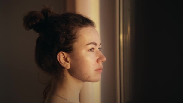 一个皮肤问题的年轻女孩的亲密的自然肖像 从窗户发出的温暖的光 女人朝旁边看去 头发集中在脑后的一个凸起处 — 图库视频影像