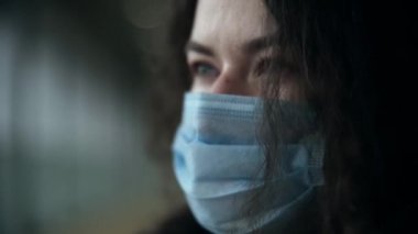 Tıbbi maske takan bin yıllık bir kadının yakın plan portresi. Rüzgar saçı geliştirir. Gözyaşları içinde üzgün gözler. Yavaş çekim serin rengi.