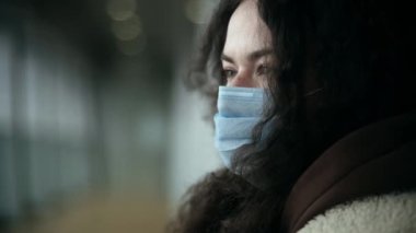 Şehir caddesinde ya da havaalanında tıbbi maske takmış bir kızın portresi. Rüzgar hareketi, nefes alma hissi. Üzgün gözler ve yalnızlık