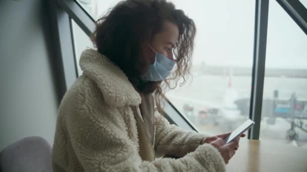 Kobieta Długimi Kręconymi Włosami Masce Medycznej Ciepłą Kurtką Siedzi Lotnisku — Wideo stockowe