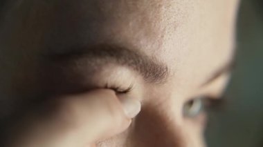 Yavaş çekim yakın çekim çerçevesi. Genç bir kadın görüşünü düzeltmek için gözlüklerini çıkarıyor. Bir parmak nazikçe göze yeni bir optik kontak lens yerleştirir. Gözden bir gözyaşı ya da lens solüsyonu sızıyor