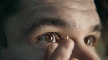 Yakın çekim yavaş çekim genç adam nazikçe kahverengi gözüne bir lens takar. Görme düzeltmesi için lens takıyorum. Güzel renk 