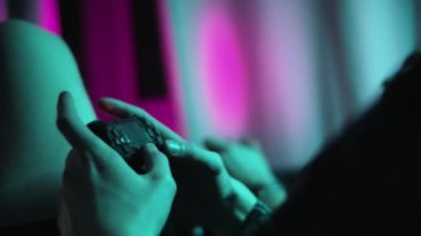 Oyun kumandası ya da oyun kumandası oyuncunun elinde. Akşam veya gece odasında iki kişi bir konsolda oynuyorlar. Bir neon ışığı oyuncuların ellerini aydınlatır.. 