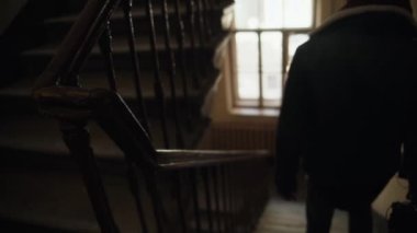 The dark figure of a silhouette of a man descends the stairs at the entrance or front door. A beautiful old staircase in an emergency house. Bad light. Problems with utilities.