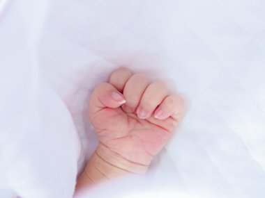 Yeni doğmuş bebek elini beyaz battaniyeye sar.