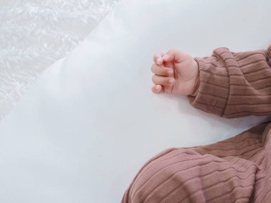 Yeni doğmuş bebek elinin yakınında beyaz yatakta kahverengi elbiseler giyiyor.