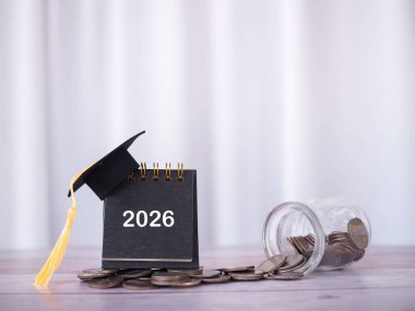 Mezuniyet şapkası ve bozuk para yığınıyla 2026 masa takvimi. 2026 yılında eğitim, öğrenci kredisi, burs, öğrenim ücreti için para biriktirme kavramı