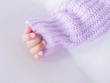 Yeni doğmuş bebeğin eli beyaz yatakta mor bir elbise giyiyor.