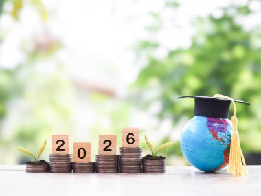 Mezuniyet şapkalı dünya küresi, 2026 numaralı tahtadan blok bozuk para yığını. 2026 yılında eğitim, öğrenci kredisi, burs, öğrenim ücreti için para biriktirme kavramı.