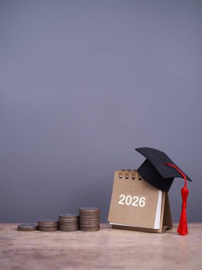 Mezuniyet şapkası ve bozuk para yığınıyla 2027 masa takvimi. 2027 yılında eğitim, öğrenci kredisi, burs, öğrenim ücreti için tasarruf kavramı