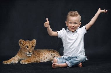 Cute kid playing with a lion cub on a black background clipart