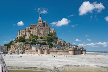 Mont-Saint-Michel güneşli bir günde mavi gökyüzü, beyaz bulutlar ve alçak gelgit.