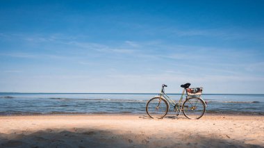 Mavi denizin üzerinde beyaz kumsalda yeşil antika bisiklet ve açık mavi gökyüzü arka planı, bahar ya da yaz tatili konsepti.