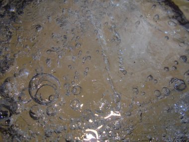 Eridikçe saydam buz makrosu çok sayıda hava kabarcığı, radyal halkalar ve ince çatlaklar gösteriyor. Nötr ışık nemli yüzeyden yansıyarak soyut bir desen oluşturur..