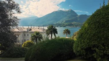 Como Gölü 'ndeki palmiye ve yeşillik boyunca kıyıdaki zarif beyaz binayı seyret. İtalyan tatil köyünün lüks mimarisi.