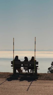 Panoramik platformda bankta oturan turist siluetleri Alp Vadisi ve ufuk manzarasına hayran kalıyorlar..