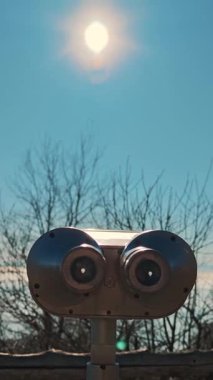 Alplerdeki panoramik platformda turist dürbünleri güneşe, mavi gökyüzüne ve çıplak ağaç dallarına karşı.