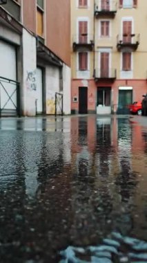 Sağanak yağış sırasında apartman binasının yağmur birikintisindeki yansıması. Su yüzeyi aynalı ıslak asfalt.