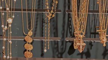 Kürsüde asılı duran yuvarlak altın madalyonlu ve haçlı kolyeler. Mücevher butiğindeki stil ve sembollerin çeşitliliği.