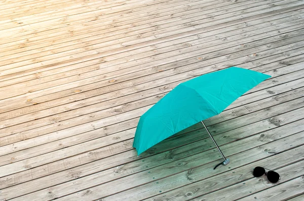 Paraguas verde con gafas de sol sobre fondo de madera en suave luz solar — Foto de Stock