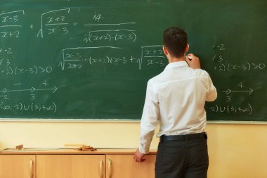 Akıllı bir genç adam, sırtı kameraya dönük bir matematik problemini çözer. Üniversite tahtasına yazı yazar..