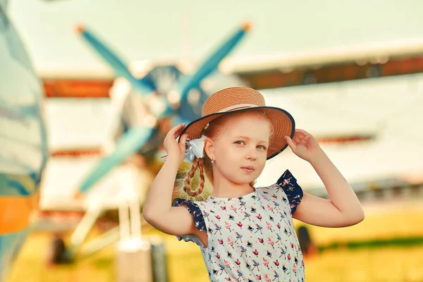 Un niño lindo en un sombrero romántico se encuentra en la pista, hélices de aviones en el fondo. El concepto de los sueños sobre viajar —  Fotos de Stock
