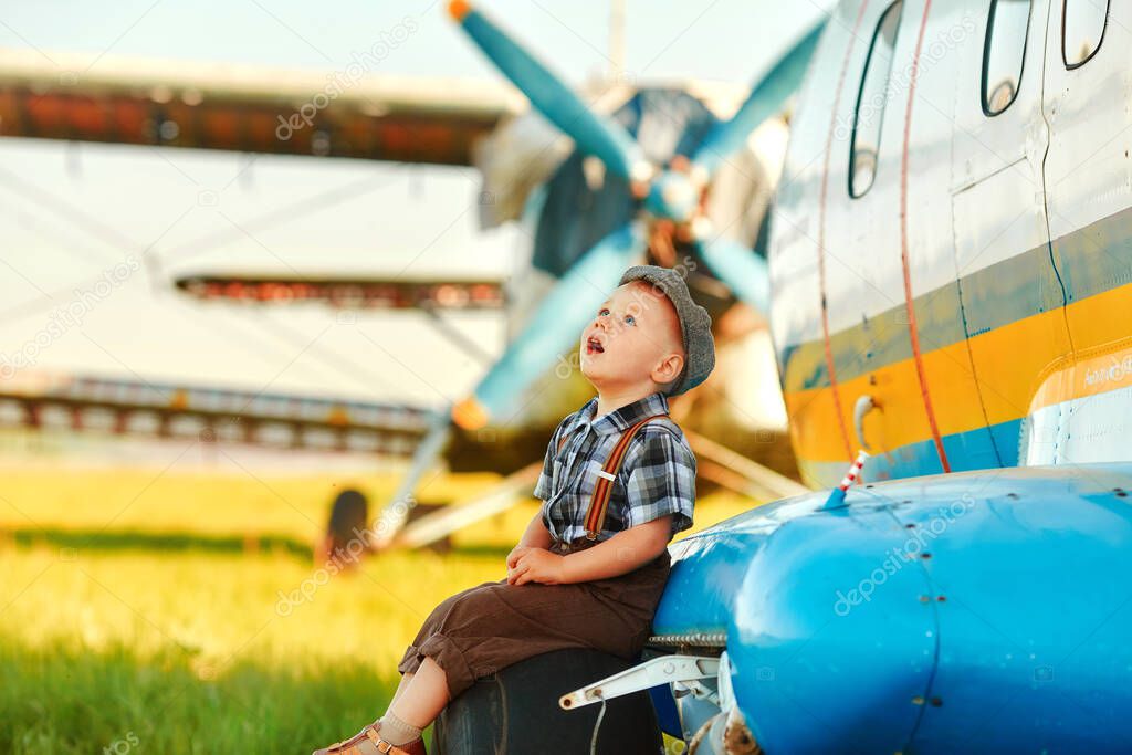 A small child sits on the landing gear wheel of an airplane and dreamily looks at the sky