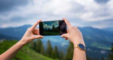 İsviçre Alplerinin resmini çekmek için akıllı telefon kamerası kullanan genç bir kadın. Yaz tatili sırasında cep telefonuyla fotoğraf çeken kadın gezgin blogcu.