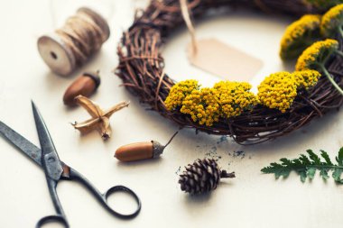 Sonbahar mahsulü kompozisyon. Sarı çiçekli çelenk, kurumuş yapraklar, meşe palamudu, kozalak, pamuk, kuru böğürtlen..