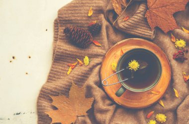 Sonbahar kompozisyonu, bir fincan bitki çayı, sıcak bir eşarp, kırsal bir arka planda kurumuş yapraklar. Sonbahar mevsimlik sıcak çay. Tatil rahatlatıcı ve sakin yaşam konsepti, kopyalama alanı. Tonu ayarlanmış resim.
