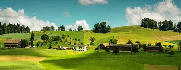 View of farm house and barn in rural area in Switzerland. Concept of organic agriculture. Colorful summer rural view of farmland. Fields and wonderful blue sky.