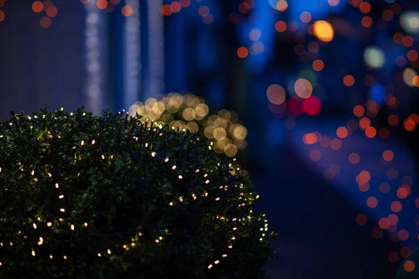 Blur of lighting in night street background. Selective focus. Christmas lights in the dark. Image of blurred background with warm colorful lights. Shopping, winter holidays.