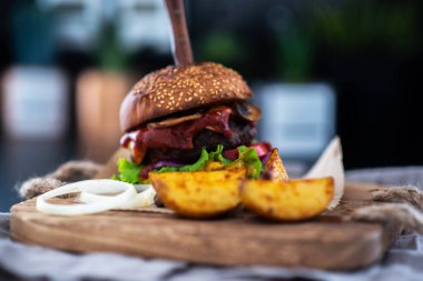 Lezzetli ızgara hamburger ve organik sebzeler. Izgara sığır eti, mantar, marul, kırmızı soğan, domates ve ahşap kesim tahtasının üzerine sos ve patates kızartması ile ev yapımı sığır eti burgeri..