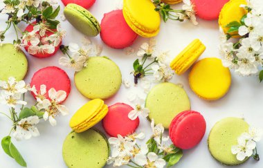 Taze bahar süslemeleri kiraz çiçekleri ve rengarenk ahşap arka planda Fransız kurabiyeleri. Fransız bademli kurabiyeleri, tatlı, üst manzara..