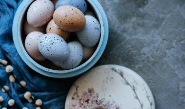 Paskalya yumurtaları, ahşap tabakta, arka planda beton kaplama. Peçete ve bahar dalları. Kopyalama alanı olan üst görünüm.