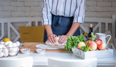 Kadın eli para kazanıyor. Un, yumurta ve diğer malzemelerle birlikte hamur, beyaz ahşap masada yatıyor. Ev yapımı pişirme işlemi.