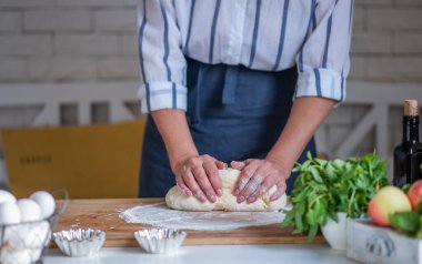 Hamur yoğuran eller, beyaz buğday unlu hamur parçaları. Düşük tuş atışı, ellere yakın çekim, masada bazı malzemeler..