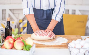 Kadın eli para kazanıyor. Un, yumurta ve diğer malzemelerle birlikte hamur, beyaz ahşap masada yatıyor. Ev yapımı pişirme işlemi.
